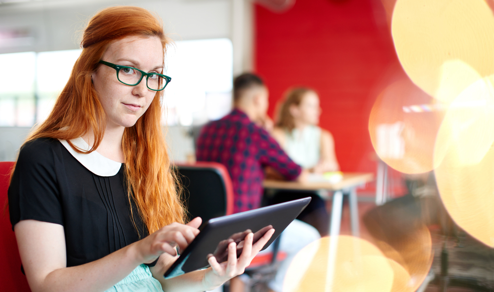 Confident female designer working on a digital tablet in red creative office space